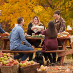 October birthday image - group of adults sitting outside eating food surrounded by barrels of apples and fall leaves
