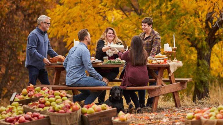 October birthday image - group of adults sitting outside eating food surrounded by barrels of apples and fall leaves