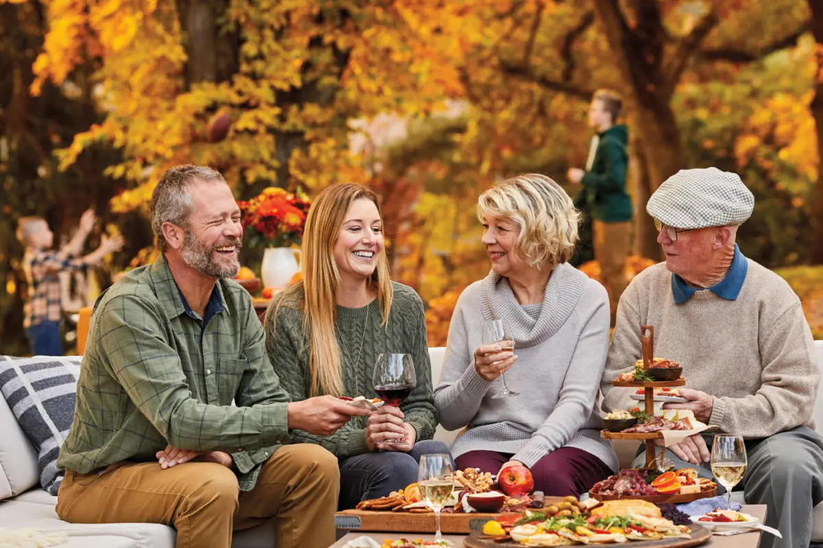 October birthday image - group of adults sitting on a couch outside drinking wine and eating finger food.