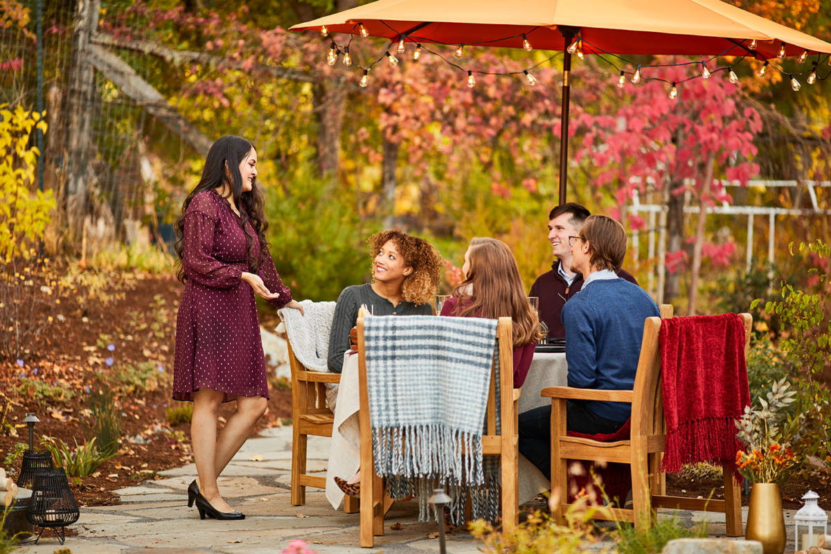October birthday image - group of people sitting outside at a table with fall leaves in the background