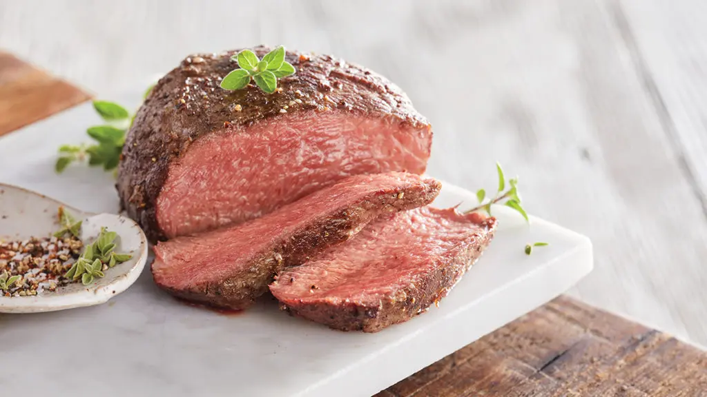 filet mignon image - sliced filet mignon on a cutting board with fresh herbs