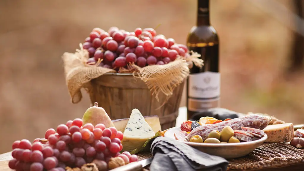 grape harvest image - grapes in baskets on a table with cured meats, cheese, and a bottle of wine.