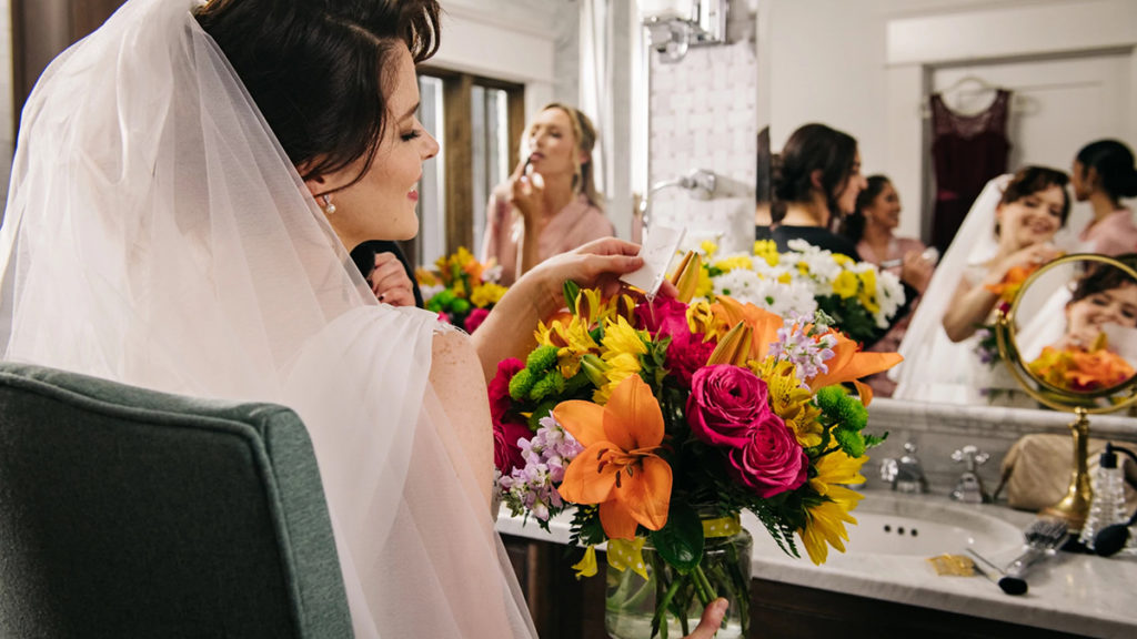 A photo of history of marriage with a bride looking at her photos while bridesmaids do their makeup in the background