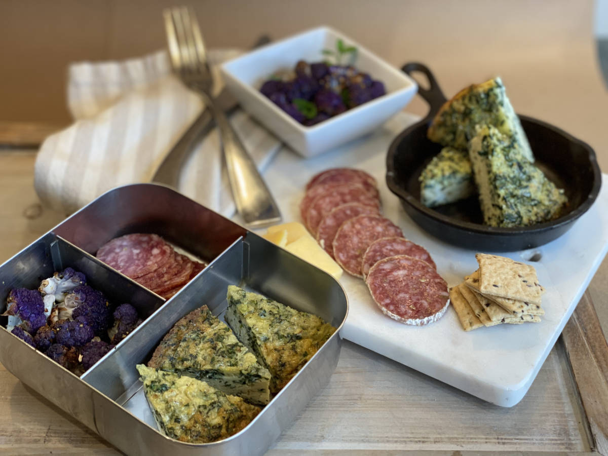 A photo of lunch box ideas, kale and cauliflower frittata on a cutting board with salami and a lunch box