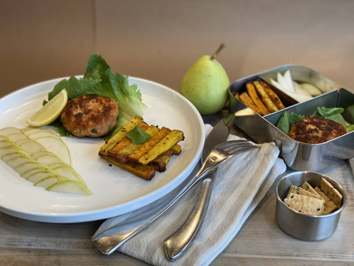 A photo of lunch box ideas, a plate with a salmon burger and pear slices next to a lunch box holding the same items.