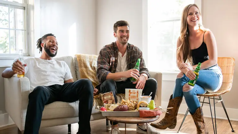 tailgate party image - three people sitting in front of a tv laughing and eating food