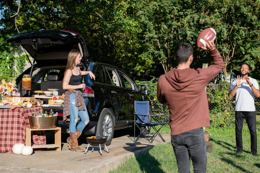 A photo about tailgate party. There's a woman woman watching two men toss a football outside.