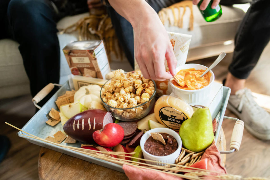 tailgate party image - snacks spread out on a board with a hand dipping a pretzel into a bowl of dip