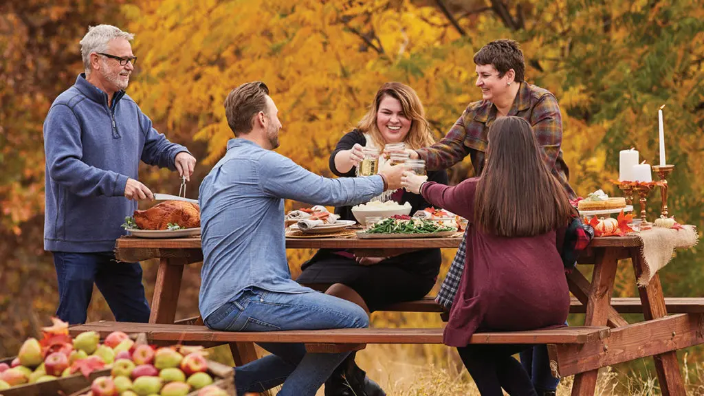 A photo of Thanksgiving dinner outside surrounded by fall leaves and barrels of apples