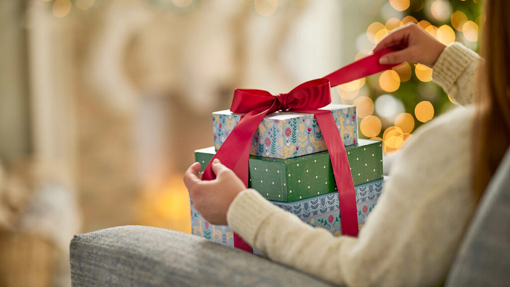 Christmas gift guide with someone unwrapping a bow on top of a pile of gift boxes.