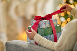 Christmas gift guide with someone unwrapping a bow on top of a pile of gift boxes.