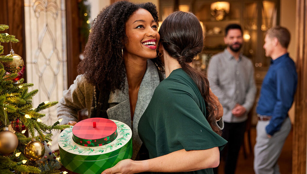 Christmas gift ideas for her with two women hugging, one holding a holiday gift.