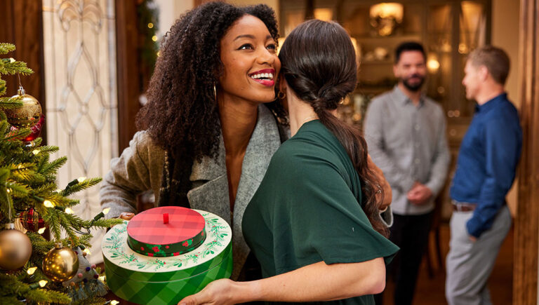 Christmas gift ideas for her with two women hugging, one holding a holiday gift.