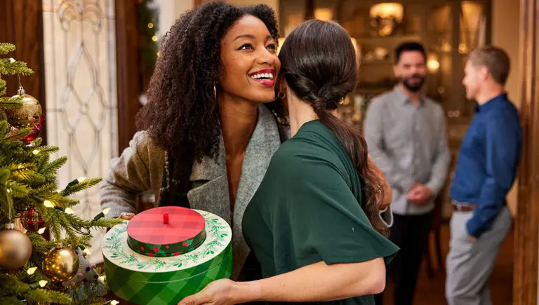 Christmas gift ideas for her with two women hugging, one holding a holiday gift.