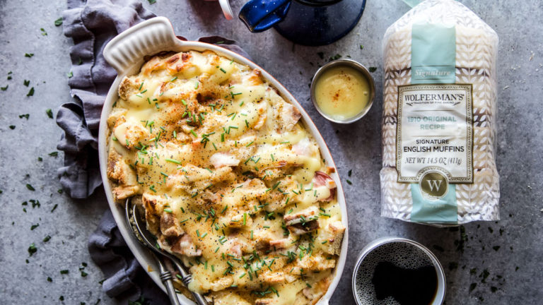 A photo of an eggs benedict casserole with a bag of English muffins and a cup of coffee next to it