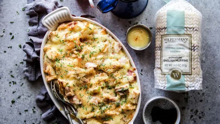 A photo of an eggs benedict casserole with a bag of English muffins and a cup of coffee next to it