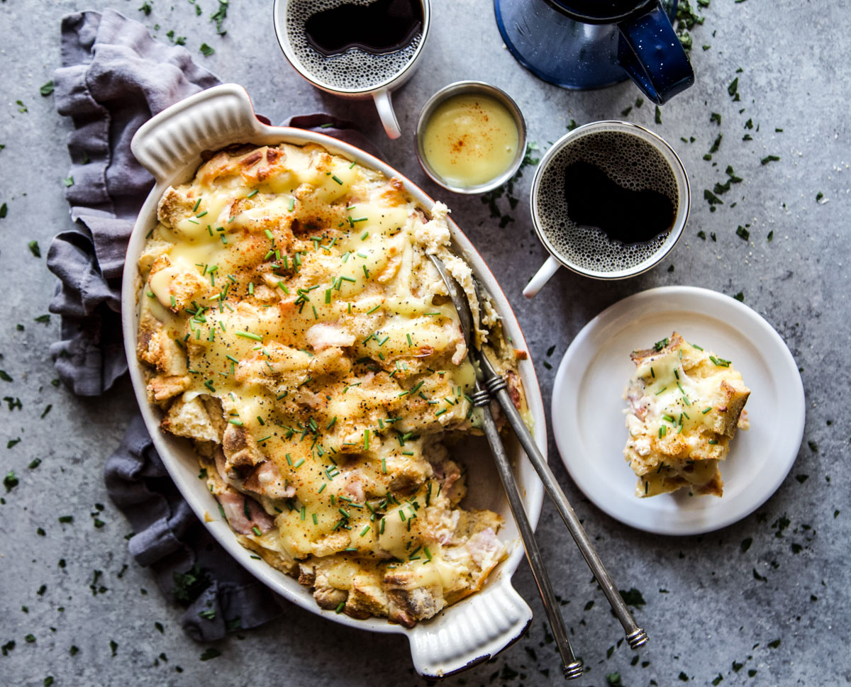 A photo of an eggs benedict casserole in a dish with a slice of the casserole on a plate next to a few cups of coffee