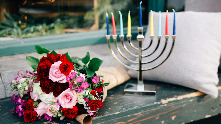 A photo of facts about Hanukkah with a menorah and a bouquet of flowers on a bench
