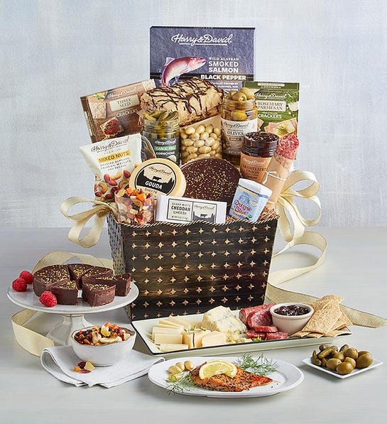 A photo of gift baskets with a basket full of cheese, smoked salmon, baklava, crackers, and other snacks with a spread of said snacks in front of the basket