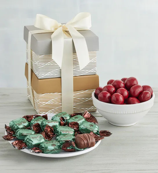 Regalos de menos de $30 esta Navidad con dos cajas de regalo apiladas una encima de la otra junto a un tazón de cerezas cubiertas de chocolate y un plato de bombones envueltos en papel de aluminio.