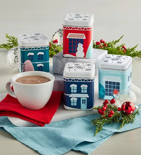 Gifts under $30 with four tins of hot chocolate decorated with holiday scenes next to a mug of hot chocolate.