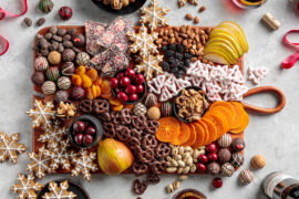 A photo of a holiday dessert board with cookies, chocolate, fruit, and nuts