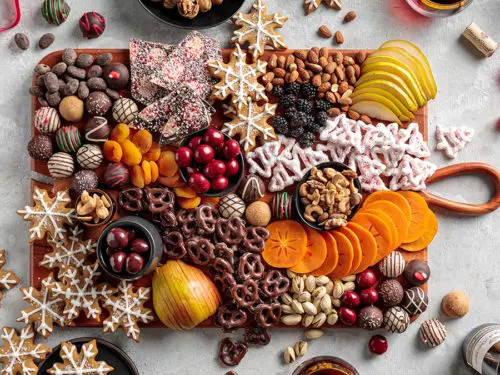 A photo of a holiday dessert board with cookies, chocolate, fruit, and nuts