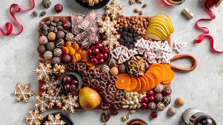 A photo of a holiday dessert board with cookies, chocolate, fruit, and nuts