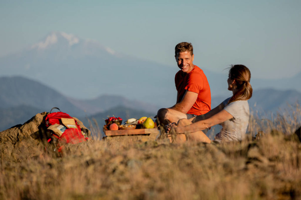 A photo of holiday shopping tips with two people sitting outside having a picnic with a mountain in the background