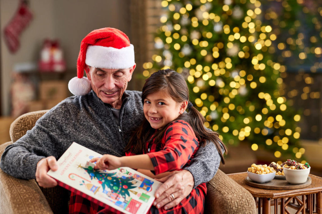 A photo of holiday shopping tips with a grandfather sitting in a chair with his granddaughter in his lap opening an advent calendar