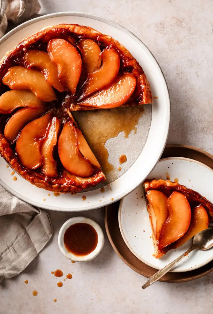 A photo of a pear tart on a plate with a slice of the same tart on a plate next to it