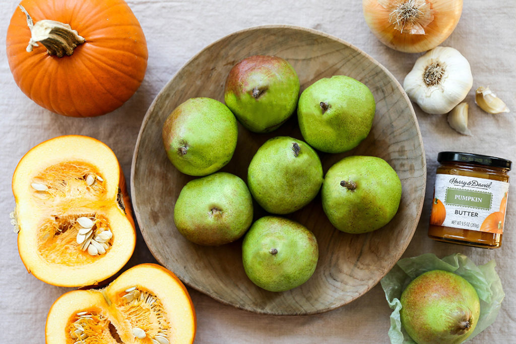 A photo of pumpkin soup with pears in a bowl surrounded by pumpkins