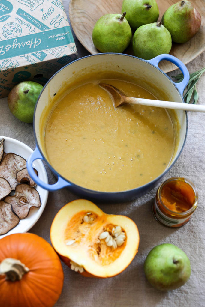 A photo of pumpkin soup with pears in a bowl surrounded by pumpkins