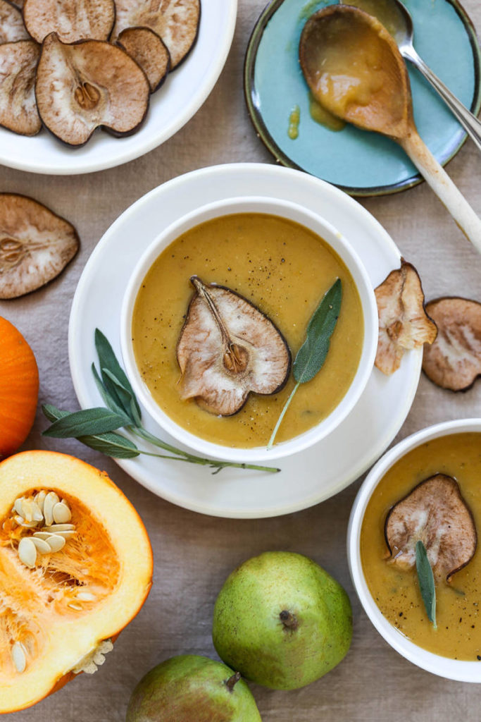 A photo of a bowl of pumpkin soup surrounded by ingredients