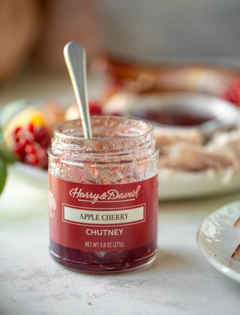 Jar of apple cherry chutney with smoked turkey in the background.