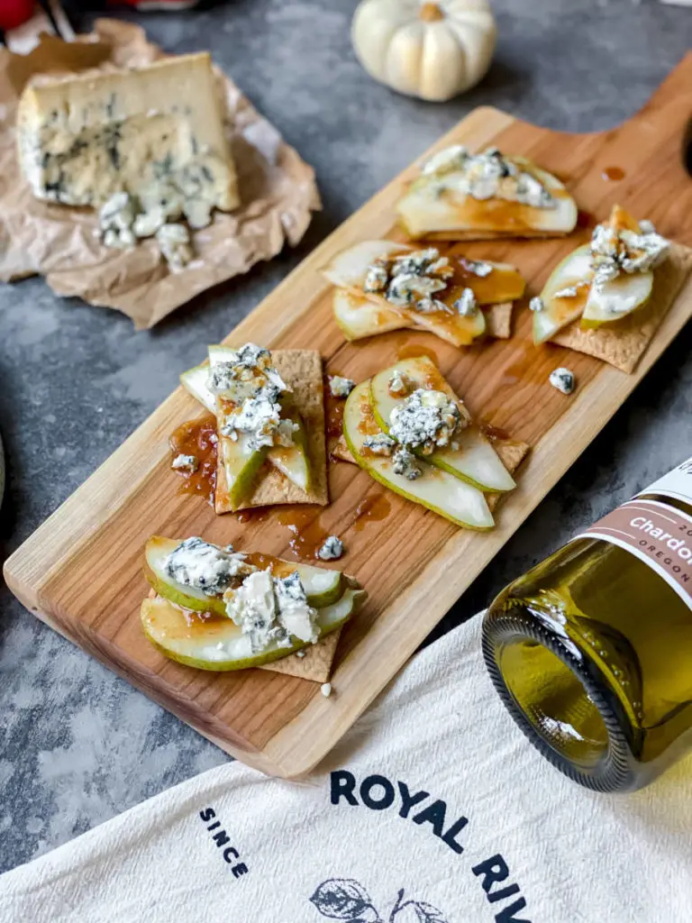 A photo of a Thanksgiving charcuterie board with sliced pears and blue cheese on crackers with a block of blue cheese in the background