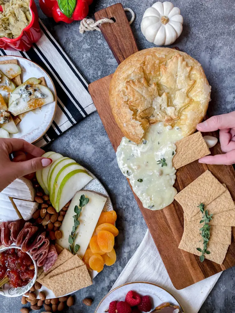 A photo of a Thanksgiving charcuterie board with two hands taking crackers and pears from the spread