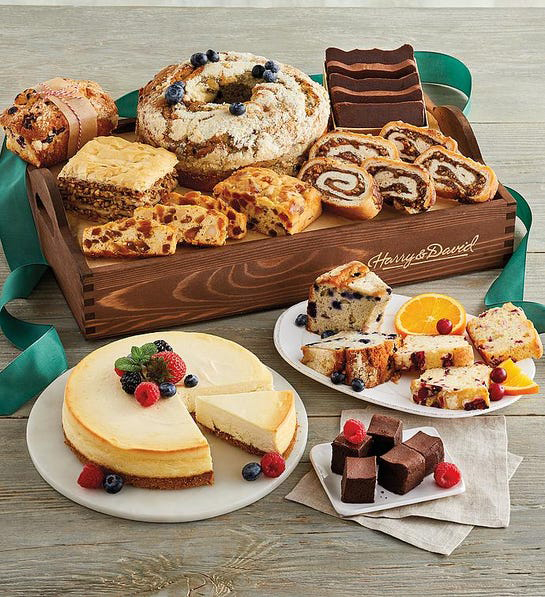 A photo of thanksgiving host gifts a box of baked goods and a cheesecake on a plate in front next to another plate full of slices of cake