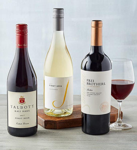A photo of thanksgiving host gifts with three bottles of wine and a full glass of red wine
