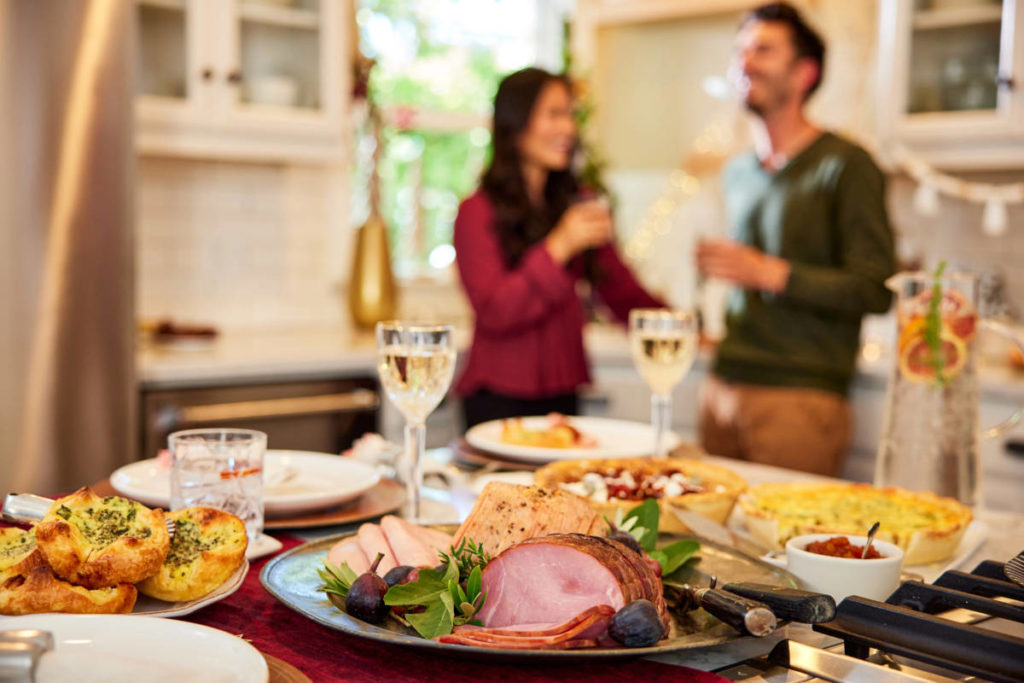 Thanksgiving host tips with a display  of food and drinks on a counter with two people talking in the background.