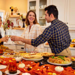 A photo of Thanksgiving tips with three people in a kitchen clinking wine glasses with a spread of food next to them