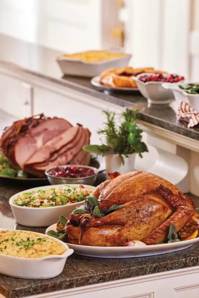 Thanksgiving host tips with a roast turkey surrounded by ham and other side dishes
