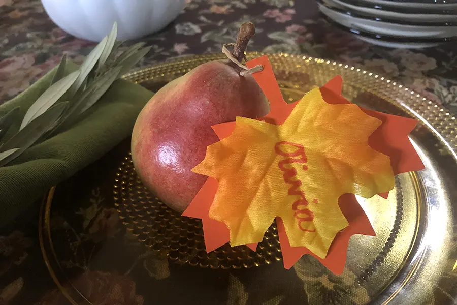 A photo of thanksgiving tree place settings with fruit on a plate and a decorative leaf with a name on it