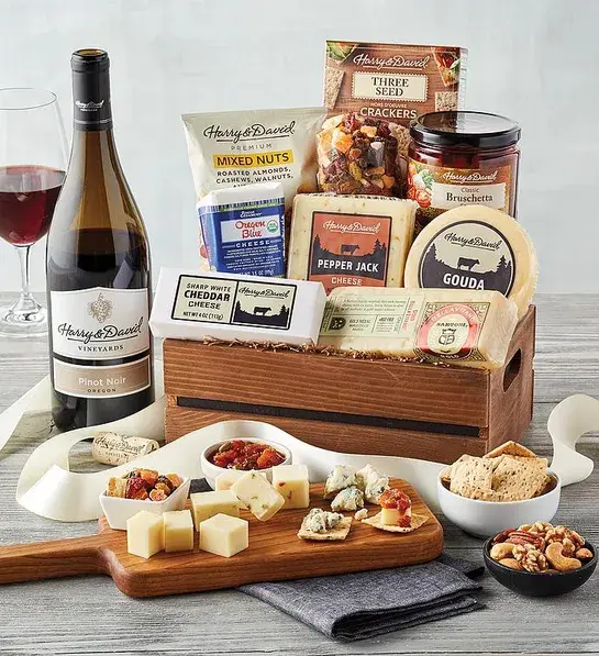Wine basket full of cheese and crackers with a bottle of wine next to it.