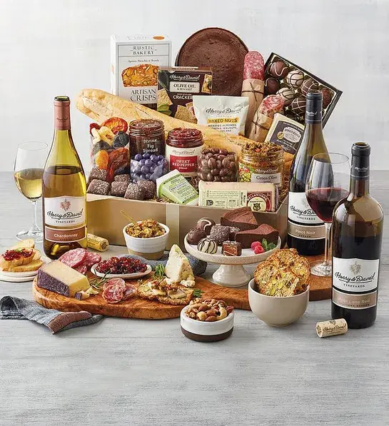 A wine basket full of cheese, crackers, chocolate treats and more surrounded by bottles of wine and the same ingredients.