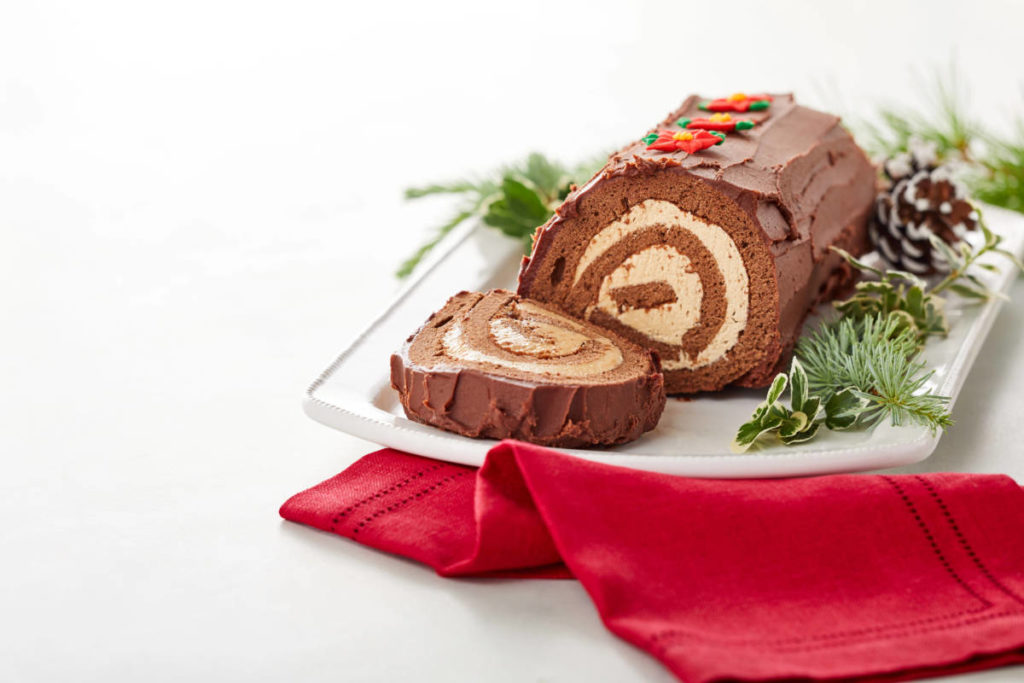 A winter solstice speciality, bûche de Noël cake sits on a platter surrounded by greenery.