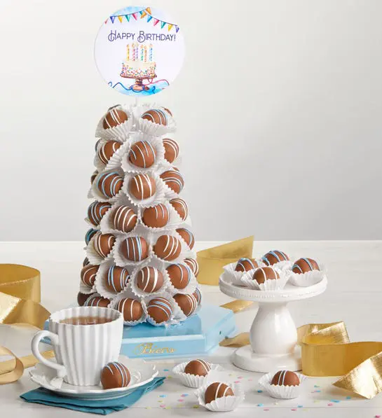 A photo of birthday gift ideas with a tower of truffles next to a plate of the same truffles and a mug of hot chocolate.