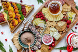 A photo of a Christmas charcuterie board with a Christmas tree shaped box full of dried fruit next to it