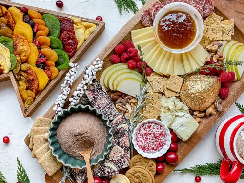 A photo of a Christmas charcuterie board with a Christmas tree shaped box full of dried fruit next to it