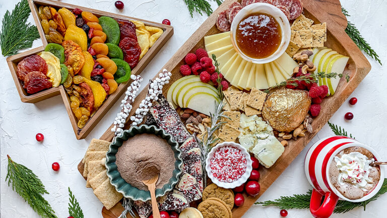 A photo of a Christmas charcuterie board with a Christmas tree shaped box full of dried fruit next to it